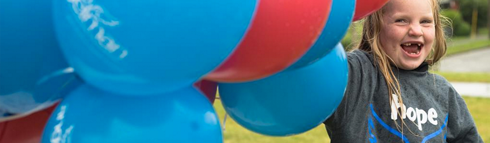 Picture of a girl with Angelman Syndrome holding a huge bunch of balloons